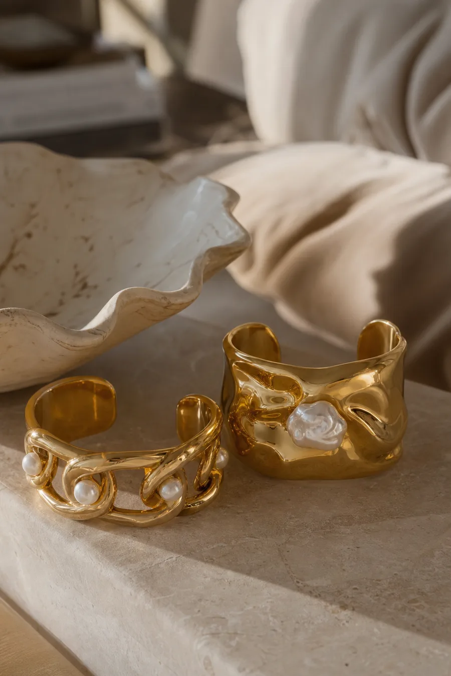 Chunky yellow gold cuff bracelets with sculptural chains and baroque pearl accents.